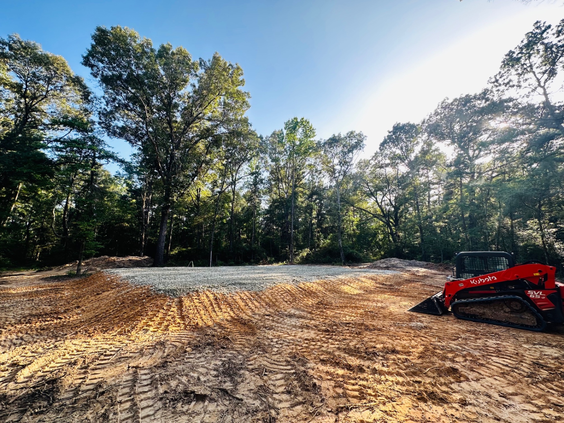 Freshly graded building pad with skid steer on a wooded Texas lot